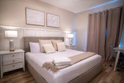 This serene bedroom features a plush light-colored bed adorned with soft pillows and a cozy blanket, complemented by stylish bedside lamps that emit a warm glow, creating a calming atmosphere for restful nights.