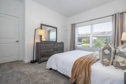This cozy bedroom, filled with natural light, offers a plush white bed adorned with textured pillows and a warm throw for your comfort. Enjoy modern decor, a sleek dresser, and large windows that frame a serene view.