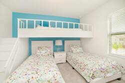 This cozy and cheerful bedroom features twin beds with vibrant floral bedding against a bold turquoise wall. A charming loft above provides extra sleeping space, and the bright natural light adds to the delightful atmosphere.