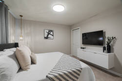 Rest in a modern bedroom with a cozy bed, soft neutral tones, pendant lighting, wall-mounted TV, white console, and simple decor, creating a calm space to relax during vacation.