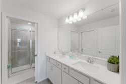 Enjoy a bright and airy bathroom featuring a sleek double vanity with plenty of counter space, modern fixtures, and a glass-enclosed shower. The clean white palette and subtle greenery create a refreshing atmosphere for your stay.