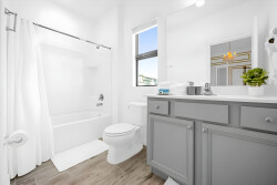 Step into a bright and airy bathroom with a modern gray vanity and stylish fixtures. The clean lines of the white tub and shower create a refreshing atmosphere, while natural light enhances the tranquil vibe throughout the space.
