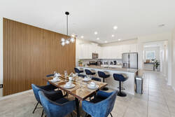 Gather in a bright dining area with a set wooden table, cozy blue chairs, modern globe lighting, warm wood accent wall, bar seating, and open access to the kitchen.