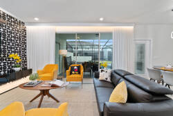 Bright yellow accents pop against the sleek black wall, creating a vibrant atmosphere in this living room. The cozy leather sofa invites relaxation, while large glass doors seamlessly connect the indoor space to the outdoors.