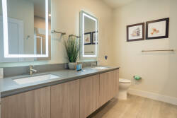 Experience a beautifully designed bathroom with a sleek dual-sink vanity and illuminated mirrors that brighten the space. The minimalist decor and subtle artwork create a serene atmosphere, ideal for relaxation.