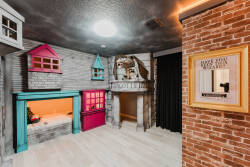 Welcome to a whimsical playroom with delightful dollhouse facades in vibrant pinks and blues, igniting creativity and fun. The warm brick wall adds charm, and the spacious layout invites endless exploration and laughter.