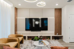 This bright and airy living area boasts a sleek flat-screen TV on a warm wood accent wall. Plush golden armchairs invite relaxation, and a modern round coffee table adds a touch of sophistication to your stay.