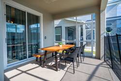 Enjoy outdoor dining in a covered screened patio with a wooden table, black wicker chairs, sliding glass doors, and natural light, creating a comfortable space for family meals during vacation.