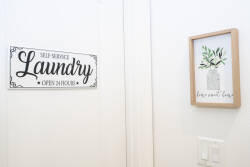 Experience a charming space where convenience meets style, featuring a "Self-Service Laundry" sign and a serene botanical print. With clean, bright walls, it's the perfect spot to refresh your vacation wardrobe.