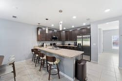 Cook with ease in a bright kitchen with dark cabinets, granite countertops, stainless steel appliances, pendant lights, and bar seating, creating a practical space for meals during your vacation.