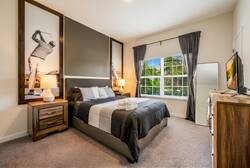 This cozy bedroom boasts a plush dark bed with fresh linens, stylish nightstands, and modern lamps that create a warm atmosphere. Large windows welcome natural light, enhancing the contemporary decor and offering a lovely view.
