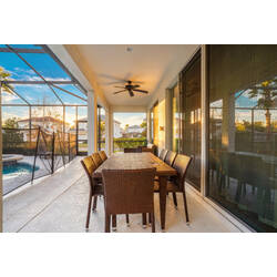 Enjoy a covered lanai with a wicker dining table, ceiling fan, and large sliding doors reflecting the pool area. Warm sunlight, outdoor seating, and peaceful views create a cozy spot for meals and relaxing Florida evenings.