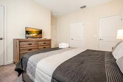 Enjoy comfort in this cozy bedroom with plush gray and white striped bedding that invites relaxation. The warm bedside lamp enhances the rich wood dresser and modern TV, creating a welcoming atmosphere for your stay.