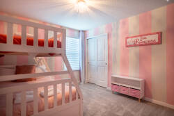 This bright and cheerful bedroom boasts a cozy bunk bed with pastel bedding and striped walls. Natural light fills the space, enhancing the playful decor and creating a warm, inviting atmosphere for a delightful stay.