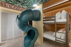 Enjoy a playful safari themed bunk room with cozy bunk beds, a fun indoor slide, jungle ceiling details, warm lighting, and soft carpet, creating an exciting space for kids during vacation.