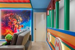 Welcome to our vibrant playroom, featuring colorful Mario-themed decor and bright blue walls that create an exciting atmosphere. Relax on the cozy gray sofa, perfect for fun-filled family gatherings and unforgettable moments.
