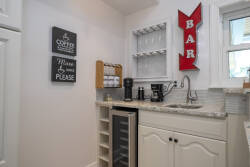 Enjoy your morning brew in this charming coffee bar with elegant white cabinetry and a stylish granite countertop. The clever wine fridge and cheerful signage create a delightful atmosphere for your stay.