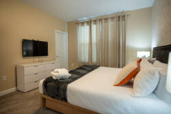 This cozy bedroom boasts a plush white queen bed with soft pillows and a stylish throw blanket, creating a restful atmosphere. Light streams through sheer curtains, enhancing the warm wall tones and inviting you to relax.