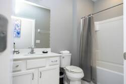 Experience a serene bathroom with a clean, minimalist design, sleek white cabinetry, and a spacious mirror that reflects natural light. The calming gray palette and modern fixtures create an inviting atmosphere for your comfort.