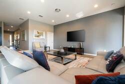 Experience a bright, airy living room with a plush sectional in soft neutral tones, vibrant throw pillows, and a sleek coffee table on a textured rug, creating a cozy atmosphere ideal for relaxation and entertainment.