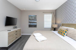 Enjoy peaceful nights in this inviting bedroom with plush bedding and a cozy geometric accent wall. A sleek dresser and mounted TV offer added convenience, while natural light fills the space for a warm, welcoming feel.