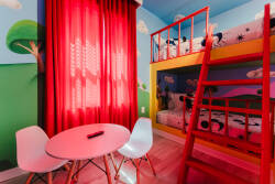 This children's bedroom boasts bright walls and a cozy bunk bed with playful bedding. Vibrant red curtains and cheerful decor inspire imagination while a small table invites games and creativity in a fun, welcoming space.