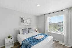 Rest in a bright bedroom with a cozy white bed, soft blue throw, gray pillows, abstract wall art, natural light, and white curtains, creating a calm space to enjoy your vacation.