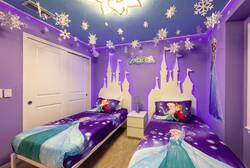 Rest in a charming Frozen themed bedroom with two cozy beds, purple walls, castle-style headboards, snowflake decor, and bright bedding, creating a magical space for kids during vacation.