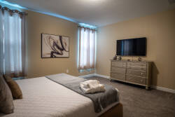 Enjoy a cozy bedroom that invites relaxation with soft, neutral tones and plush carpeting. The stylish dresser and modern artwork complement the natural light from sheer curtains, creating a serene atmosphere for your stay.