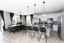 This stylish kitchen boasts sleek stainless steel appliances and a spacious island with modern bar stools, ideal for casual meals and socializing, while large windows invite natural light, enhanced by elegant dark curtains.
