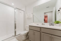 This bright bathroom offers a sleek glass shower and a spacious vanity with soft gray cabinetry, perfectly enhancing the light decor. Fresh greenery and modern fixtures add a refreshing touch for your comfort.