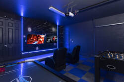 Enjoy a lively entertainment room with stylish black seating and dynamic blue lighting, ideal for movie nights or gaming marathons, featuring a large screen for immersive viewing and a foosball table for some friendly fun.