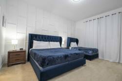 Enjoy restful nights in this beautifully designed bedroom with plush blue velvet beds for ultimate comfort. The soft beige carpet enhances the modern decor, and natural light pours in through the crisp white curtains.