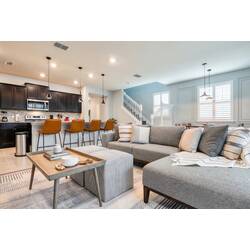 Stylish and contemporary, this living area features a cozy sectional sofa adorned with textured pillows and a chic coffee table, while the warm wooden bar stools invite you to enjoy moments in the sleek kitchen just steps away.