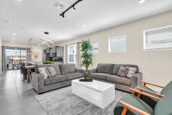 This bright living area boasts inviting gray sofas, a stylish white coffee table, and warm wooden accents. Large windows enhance the space, showcasing vibrant surroundings and creating a welcoming atmosphere for your relaxation.