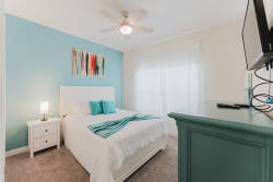 Unwind in this cozy bedroom adorned with calming colors and vibrant artwork. Enjoy the soft bedding and fresh blue accent wall, while natural light filters through sheer curtains, creating a welcoming and peaceful atmosphere.