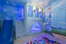 Enter a whimsical playroom filled with vibrant castle murals and a fun slide for adventure. Enjoy the cozy, colorful carpeting and soothing blue lighting that create a magical atmosphere ideal for imaginative play.