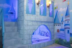 Step into a whimsical sanctuary featuring a charming castle-like structure with vibrant blue accents and enchanting wall murals. The cozy nook invites relaxation, perfect for settling in after a day of adventure.