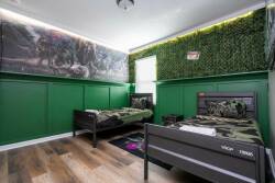 Welcome to a playful haven for adventure, where two twin beds with camouflage bedding sit against vibrant green walls. The lively mural and touches of greenery enhance the energizing atmosphere for your stay.