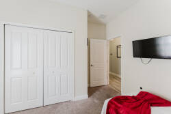 This cozy bedroom features plush carpet underfoot and a soft, inviting red throw draped over the bed. With ample closet space and a mounted TV, it’s designed for both relaxation and convenience, making your stay effortless.