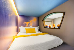 Enjoy a cozy retreat in our uniquely designed bedroom, featuring a vibrant mural, soft blue ceiling, inviting queen bed with crisp linens, a cheerful yellow throw, and a stylish mirror for added charm.