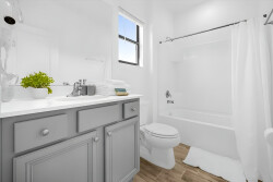 This bright and airy bathroom boasts a sleek gray vanity and a white countertop, creating a fresh atmosphere. Natural light floods the space, highlighting the modern fixtures and inviting you to relax and unwind.