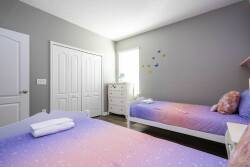 This bright and cheerful bedroom offers two cozy beds with vibrant ombre bedding, creating a playful atmosphere. Soft natural light fills the space, highlighting smart storage and charming decor for a truly relaxing stay.