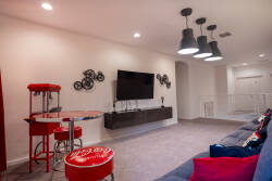 Welcome to our lively entertainment space, featuring a vibrant red bar table and stylish stools, ideal for casual gatherings. Enjoy the inviting atmosphere with a sleek wall-mounted TV, unique decor, and modern pendant lighting.