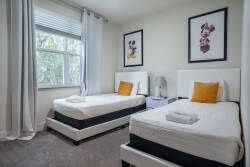 Bright and cheerful, this cozy room features two twin beds adorned with crisp white linens and playful accents. Large windows allow natural light to fill the space, complemented by charming artwork that adds a touch of whimsy.