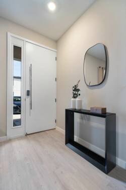 Step into a bright, airy entryway filled with natural light and sleek lines. A minimalist black console table, chic mirror, and subtle greenery set a stylish tone, while a modern door adds sophistication to your experience.