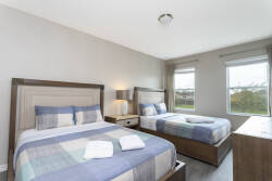 Bright and airy, this bedroom features two cozy beds with soft, plaid bedding that invites relaxation. Large windows frame a lovely view while warm wood accents and neatly arranged accessories create a tranquil atmosphere.