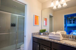 Enjoy a beautifully designed bathroom with sleek granite countertops, fresh towels, and vibrant contemporary artwork. The modern fixtures and spacious shower offer a refreshing and inviting atmosphere for your comfort.