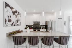 Welcome to this stylish kitchen featuring sleek quartz countertops and modern cabinetry. The spacious island, ideal for casual meals or morning coffee, is beautifully lit by warm pendant lights, complemented by charming art for a.