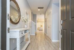 Welcome to a bright hallway with light wood flooring and soft gray walls. A charming console table with fresh flowers and a round mirror invites you to explore and feel at home. Enjoy your stay!